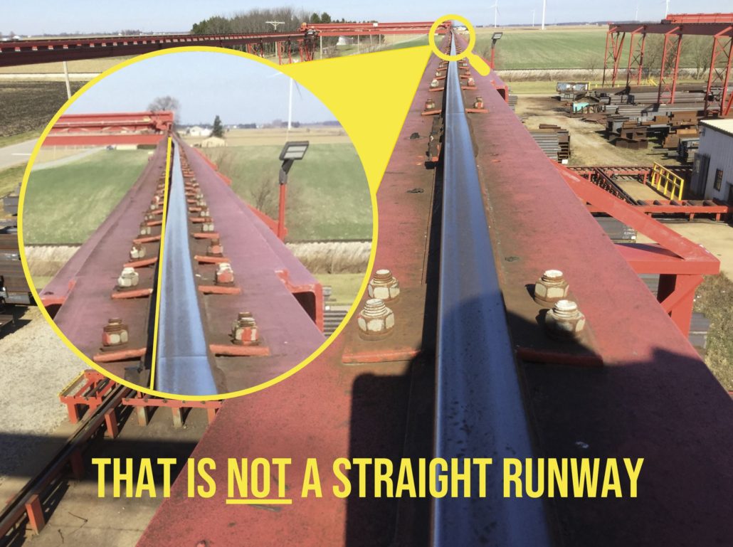 A red runway built for an overhead bridge crane system which needs maintenance, as inspected by Harriman Material Handling service technician is pictured highlighting the curvature of the runway itself, noting in yellow text, "that is NOT a straight runway."