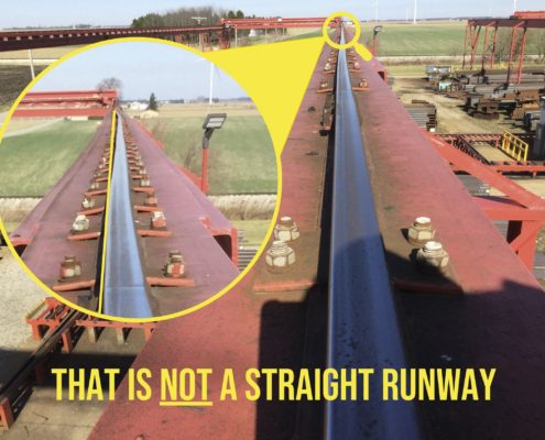 A red runway built for an overhead bridge crane system which needs maintenance, as inspected by Harriman Material Handling service technician is pictured highlighting the curvature of the runway itself, noting in yellow text, "that is NOT a straight runway."